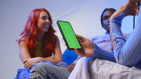 Close-Up-Of-Woman-With-Green-Screen-Mobile-Phone-Sitting-With-Gen-Z-Friends-Talking-And-Sharing-Posts-5